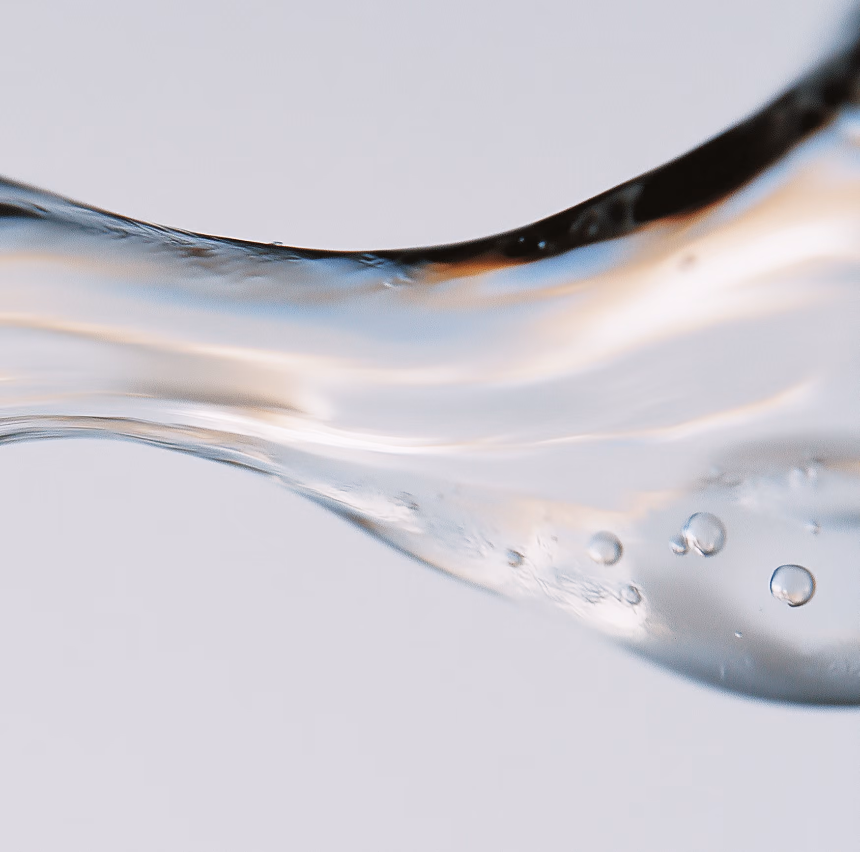 Close-up of a curved clear liquid flow with air bubbles inside against a light background.