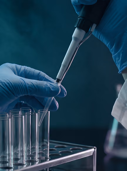 Gloved hands using a pipette to transfer liquid into a test tube in a laboratory setting.