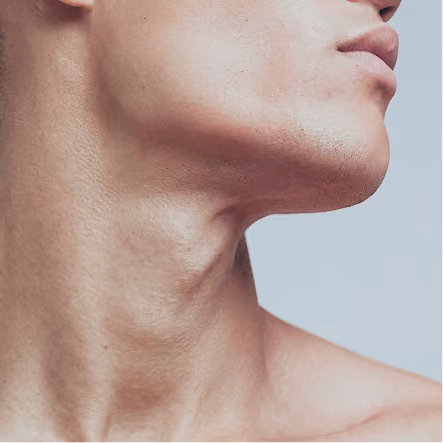 Close-up of a person's jawline, neck, and partial lips against a plain background.