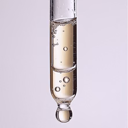 Close-up of a dropper with clear liquid and bubbles inside against a light background.
