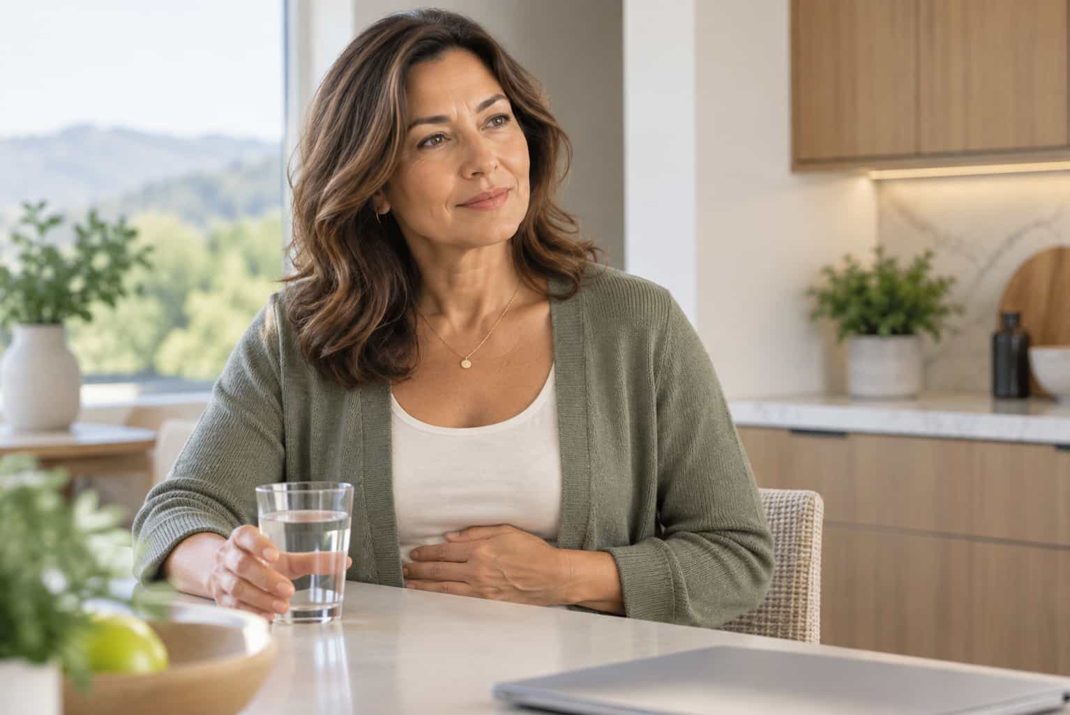 Woman seated at a kitchen table with water for the Ultimate Guide to Gallbladder Surgery.