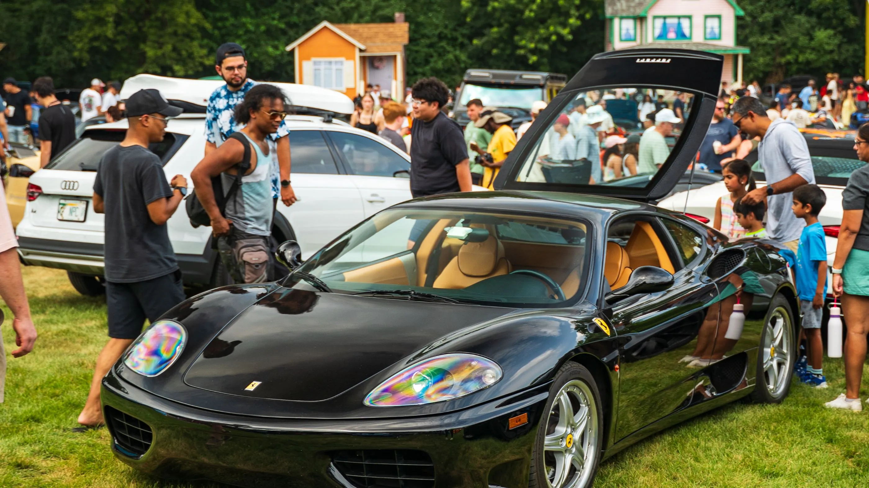 Guests in everyday dress gathered around a black Ferrari on the grass