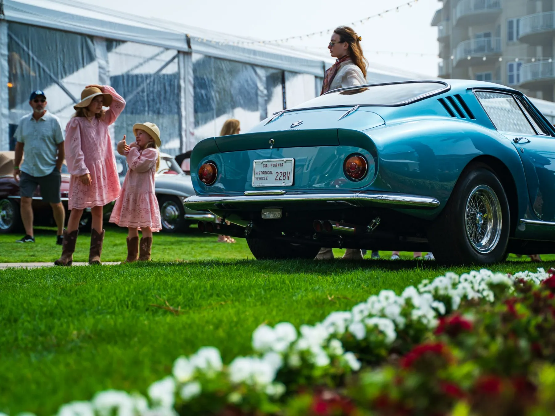 A mother and two children walking past a classic sports car on the lawn