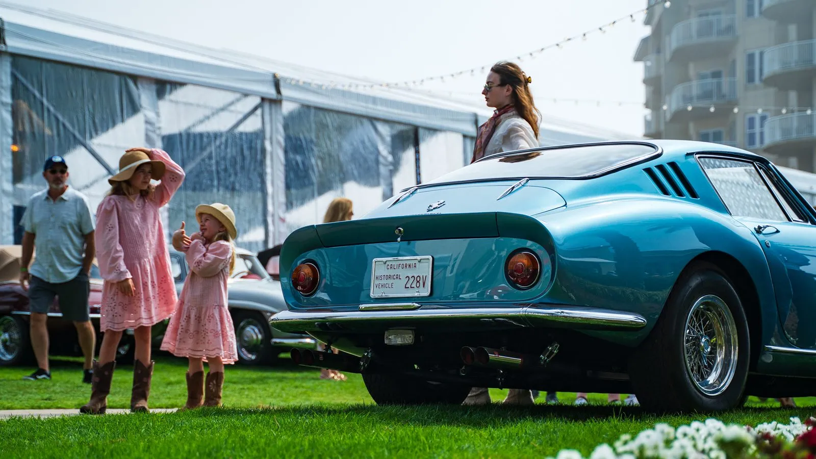 A family with two children walking past a classic Ferrari on the show lawn