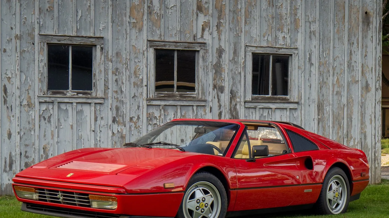 A red Ferrari 328 parked beside a weathered barn