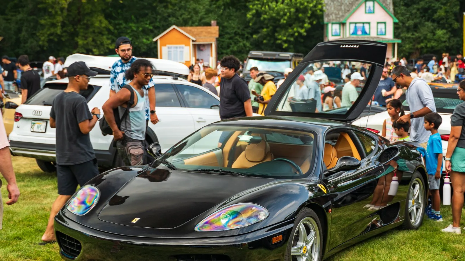 A black Ferrari 360 on the grass with visitors moving between the show cars