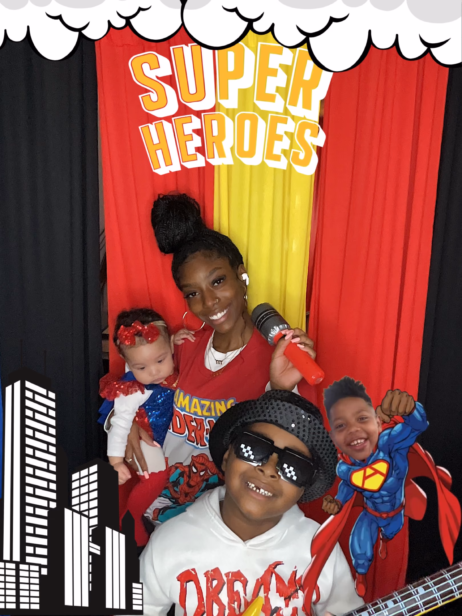 Smiling woman holding a baby and a microphone with a boy in sunglasses and a superhero cartoon boy.