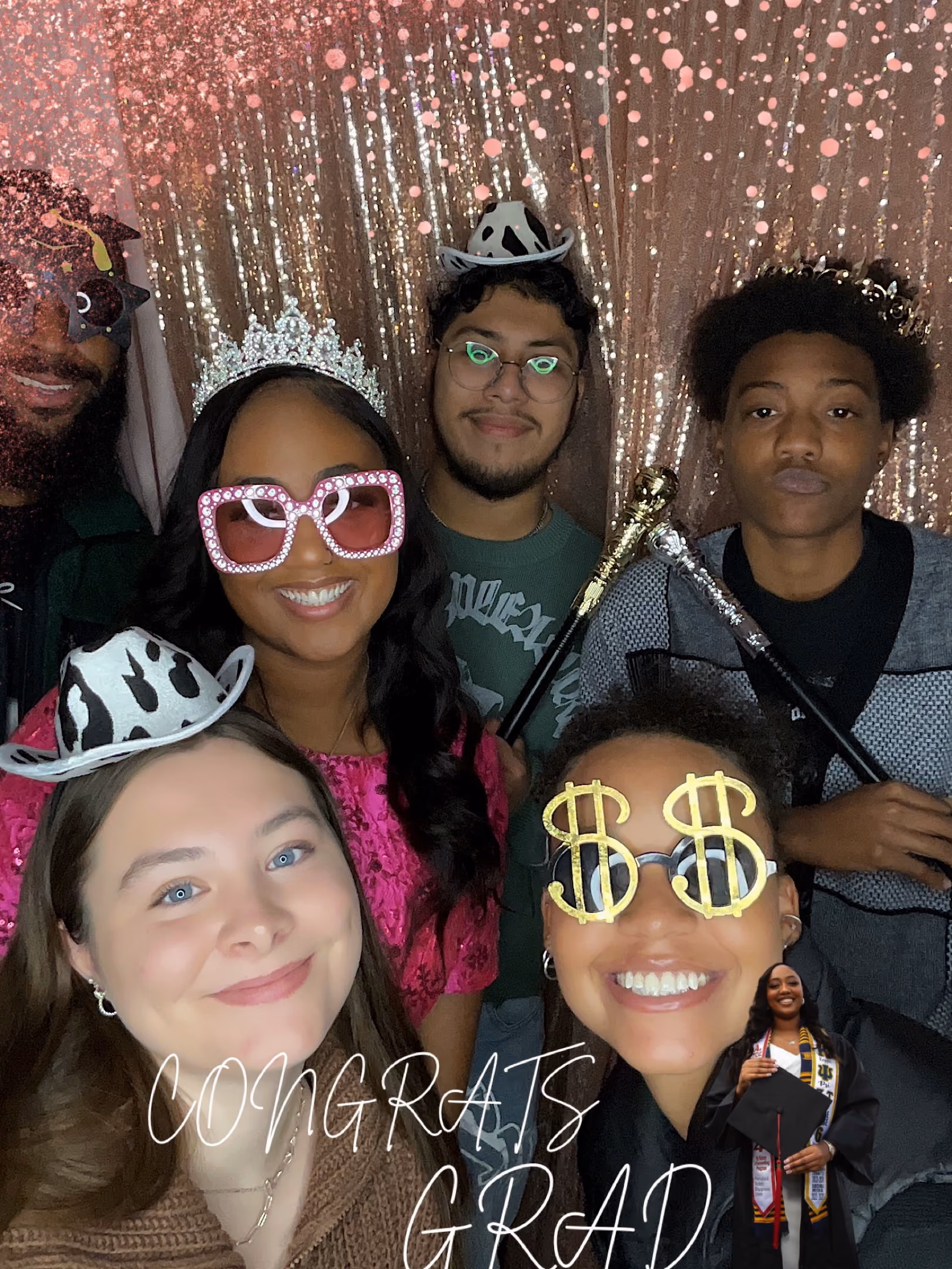 Group of smiling diverse young adults wearing fun hats and glasses in front of sparkling backdrop.