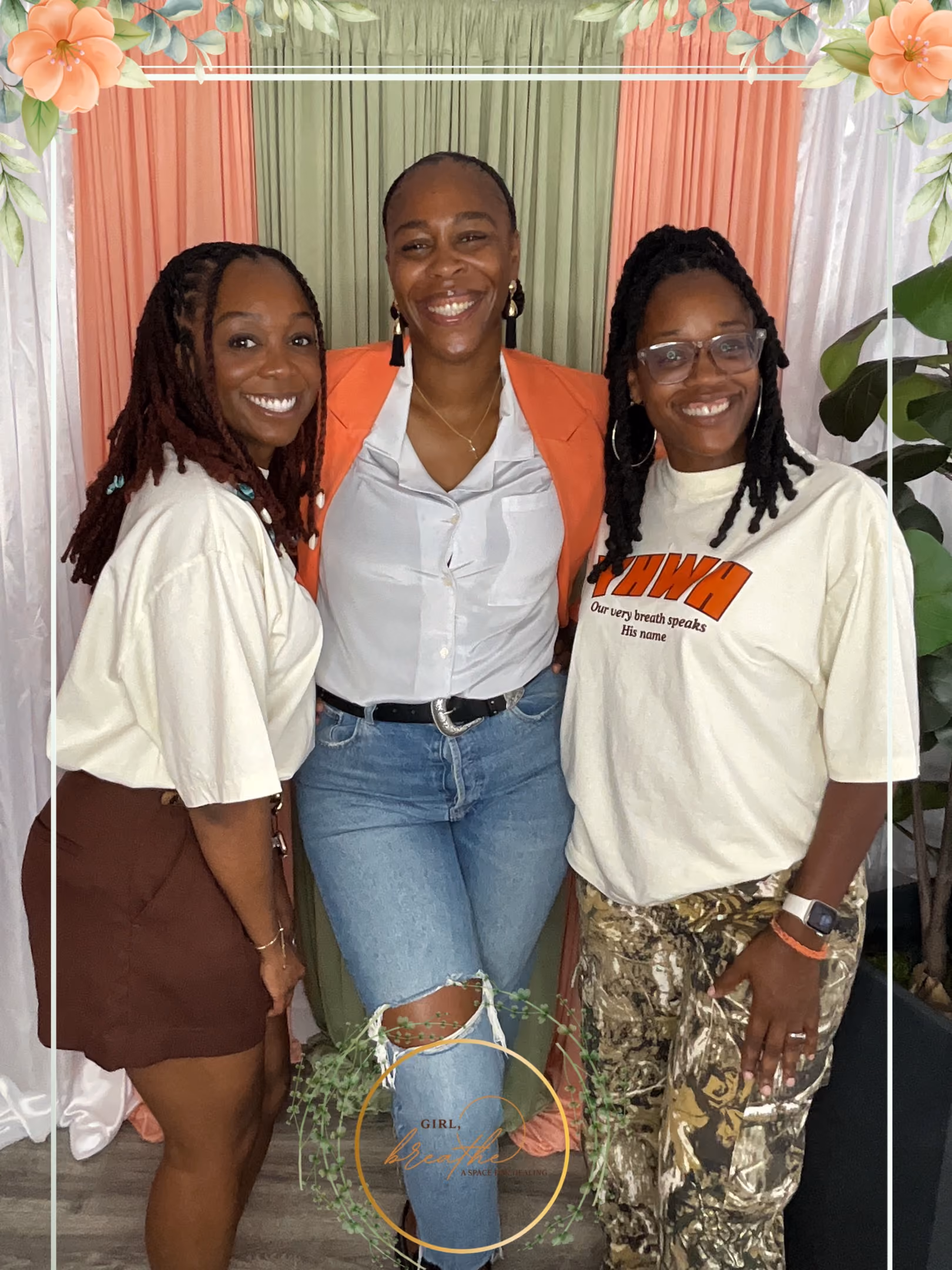Three smiling women standing together in front of pink, green, and white draped backdrop with flowers.