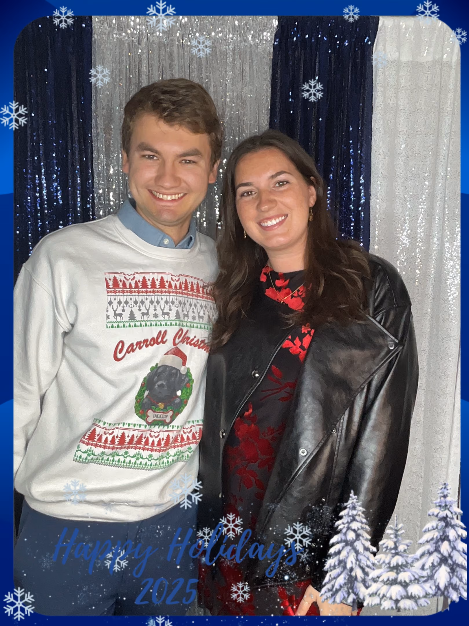 Smiling man and woman posing in front of silver and blue holiday backdrop with snowflake edges.