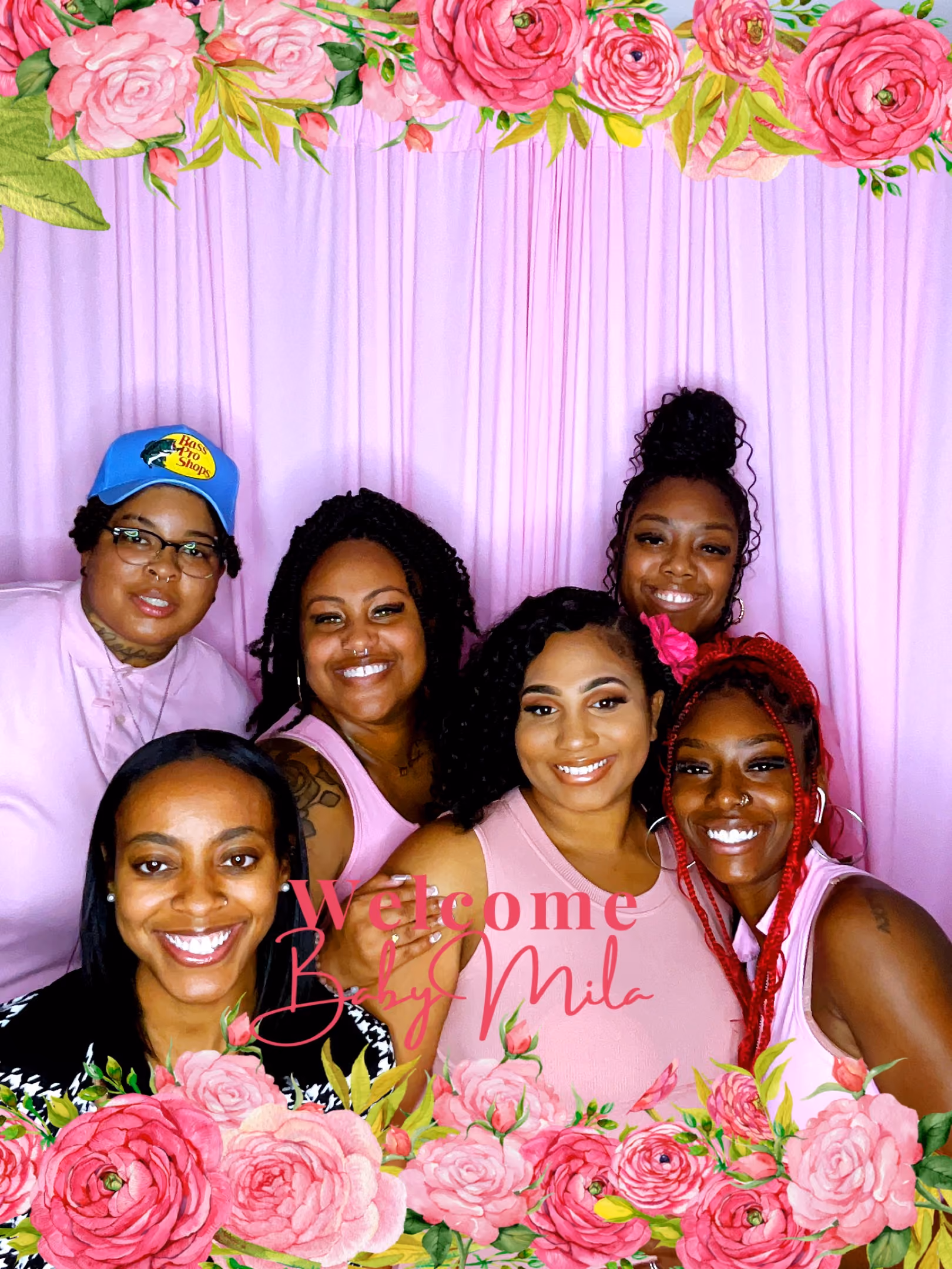 Six smiling women posing in front of a pink backdrop with floral borders and the text 'Welcome Baby Mila'.