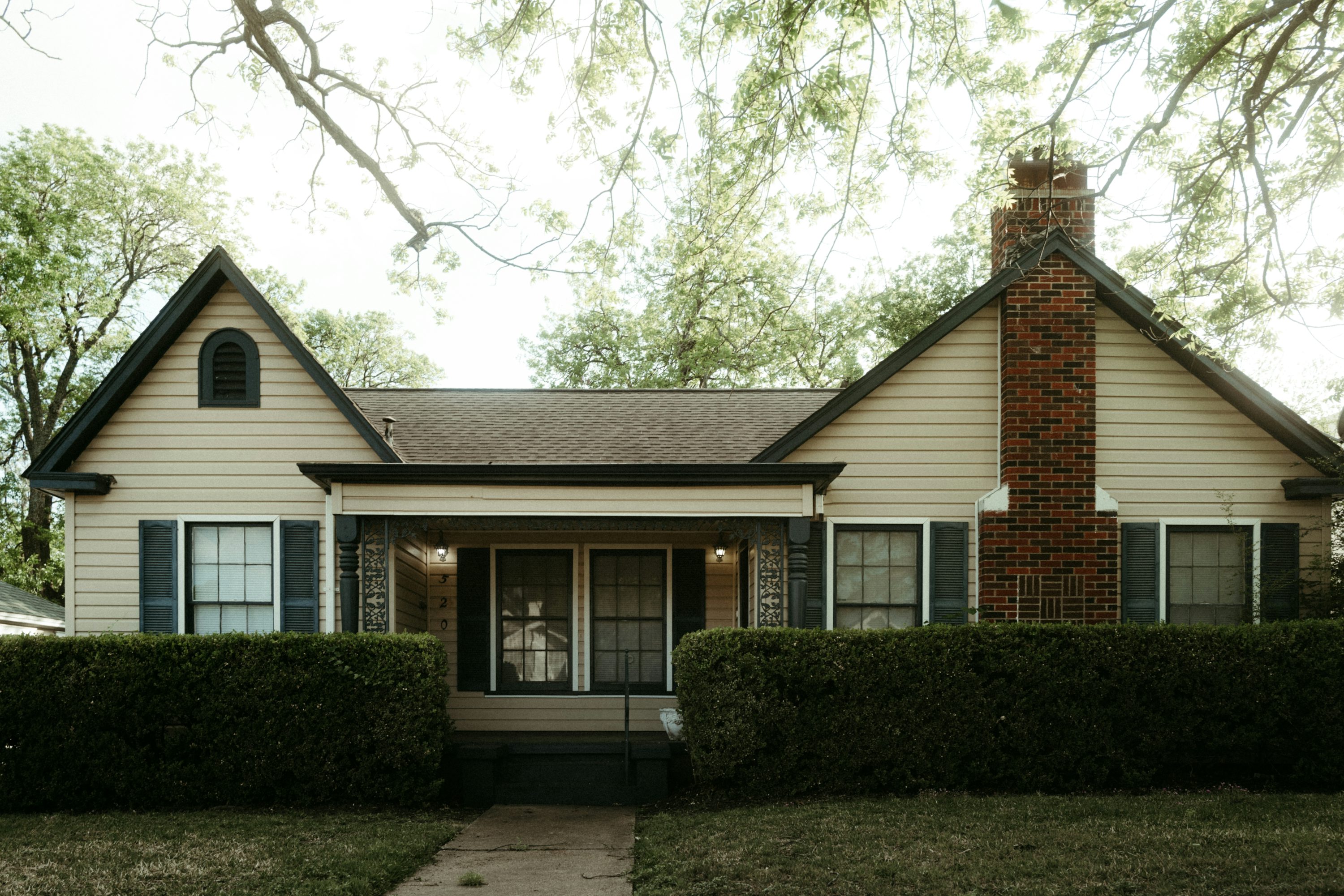 Tall red brick chimney rising above the roofline of a cream-sided single-story house with green shutters