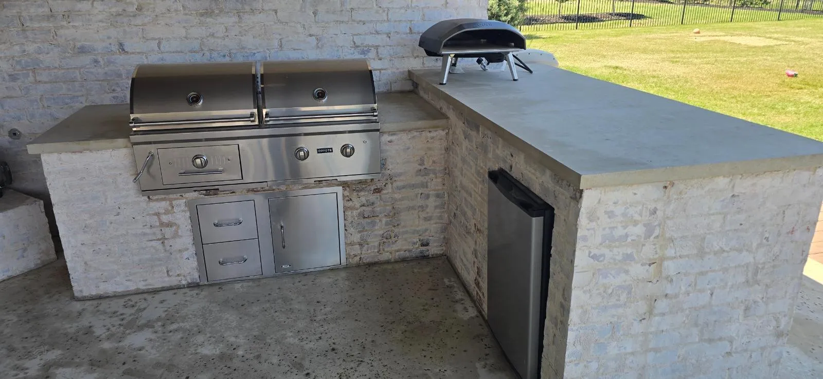 Outdoor kitchen island with a built-in stainless grill, pizza oven and refrigerator after a cleaning