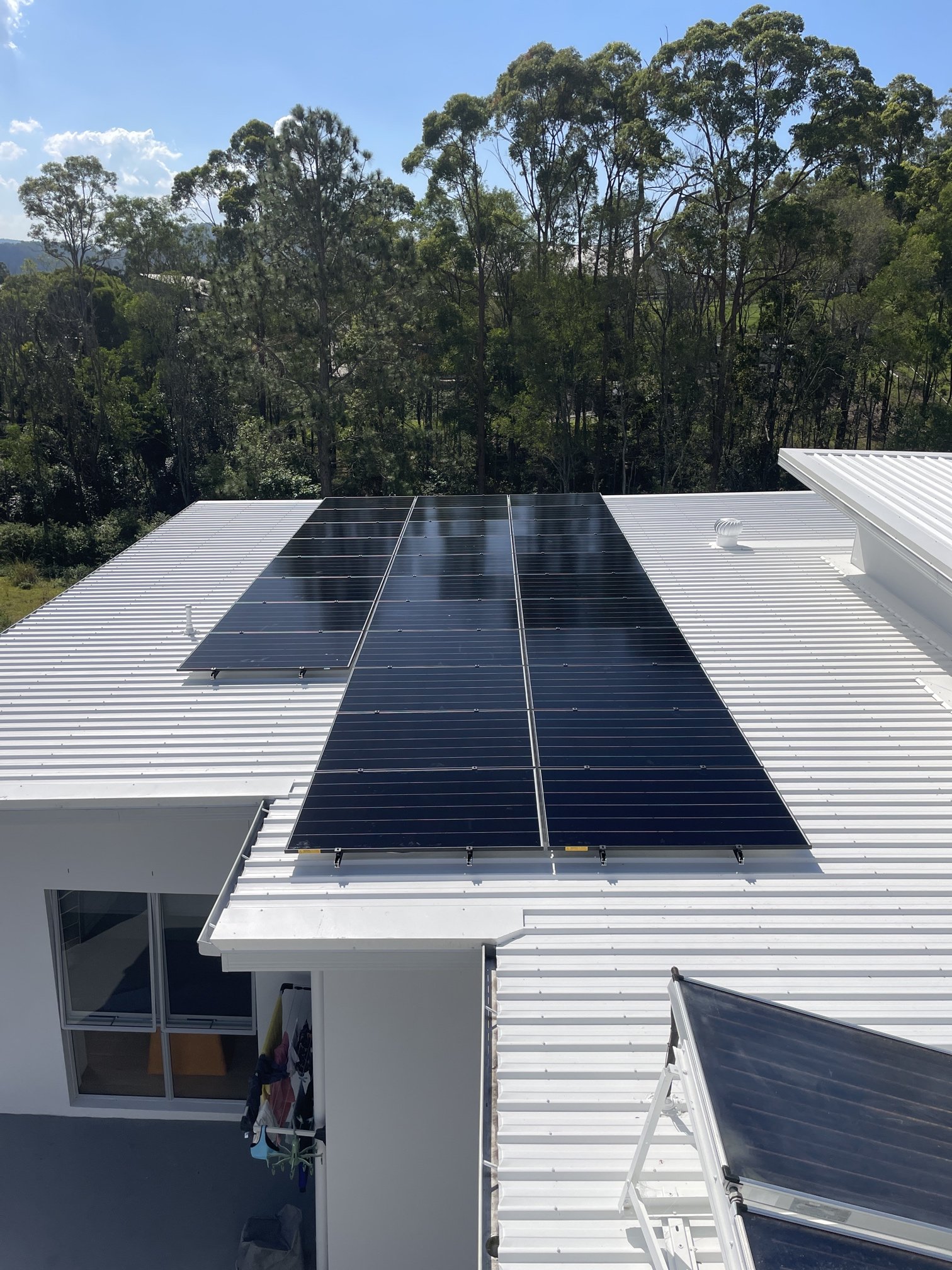 Black solar panels on a white metal roof at a Maudsland home with bushland behind