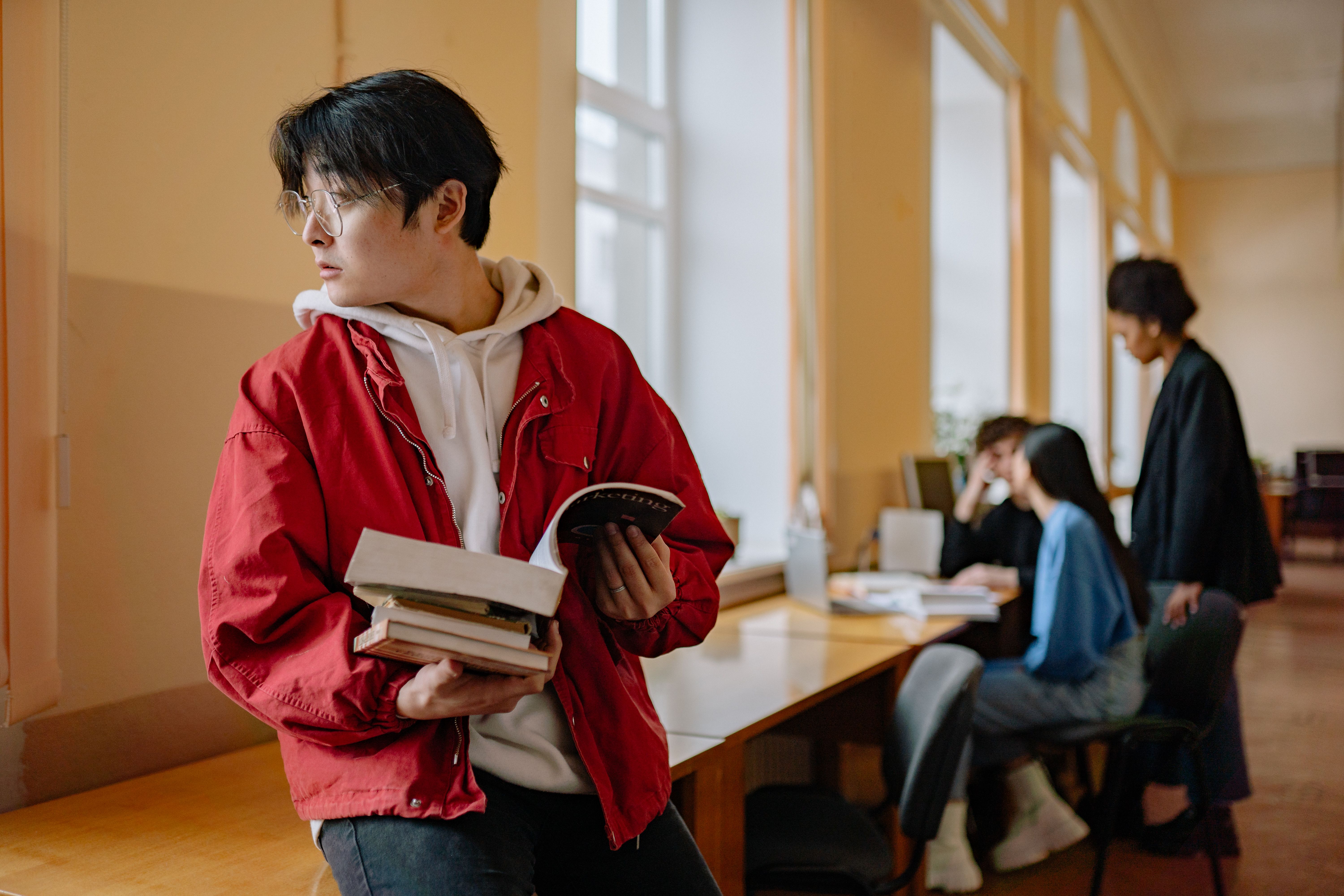 male high school student reading a book in a school library while looking out the window