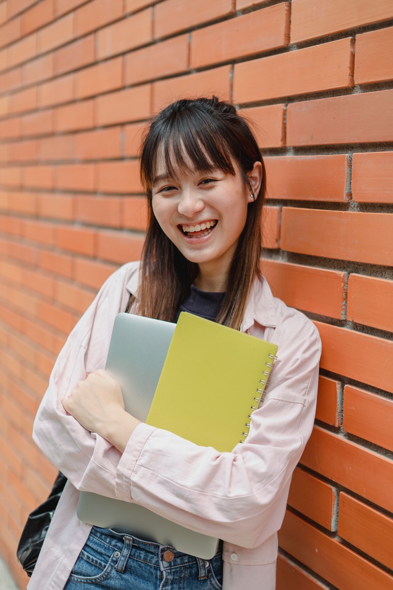 high school student leaning against a brick while and smiling while holding textbooks