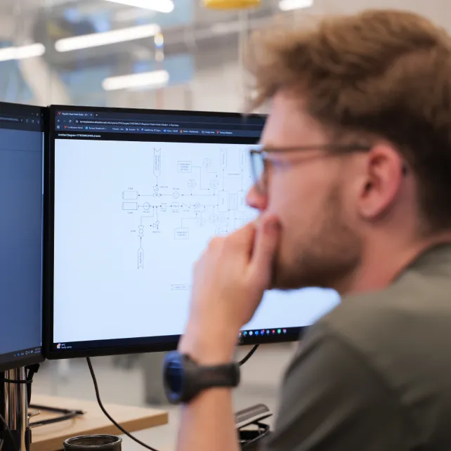 Man with glasses and smartwatch studying a technical diagram on a computer monitor in an office.
