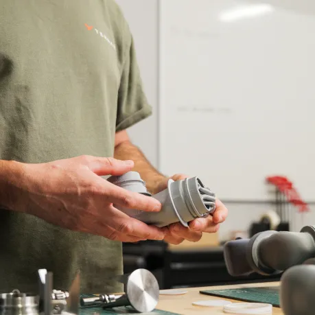 Person in green shirt holding a gray 3D printed mechanical part over a workbench.