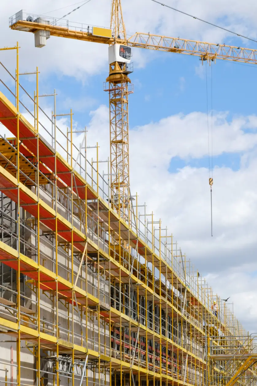 Yellow scaffolding surrounds a building under construction with a tower crane overhead against blue sky.