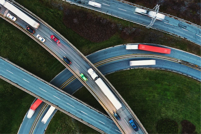 Aerial view of vehicles including trucks and cars on intersecting highways with green areas below.