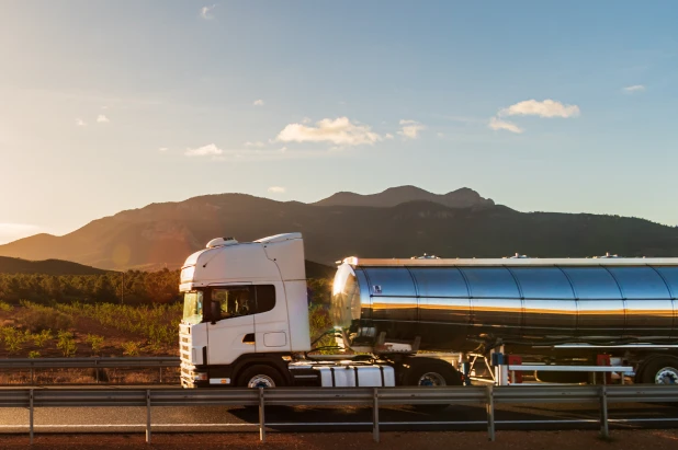 White tanker truck driving on highway with mountains and sunset in the background.