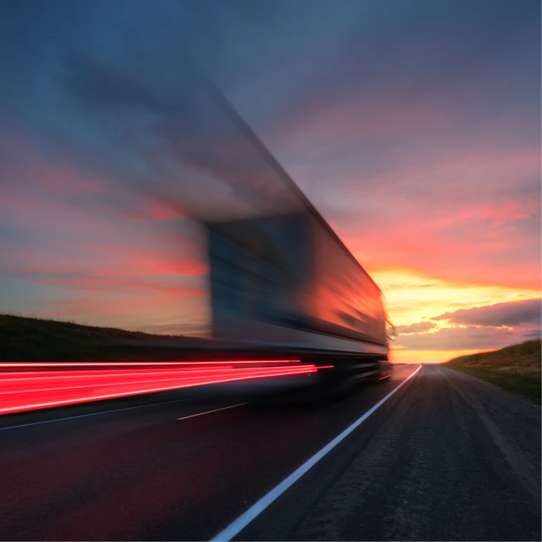 Blurred truck speeding on road with light trails at sunset under colorful sky.