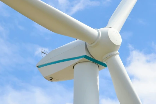 Close-up of a white wind turbine spinner and three blades against a partly cloudy blue sky.