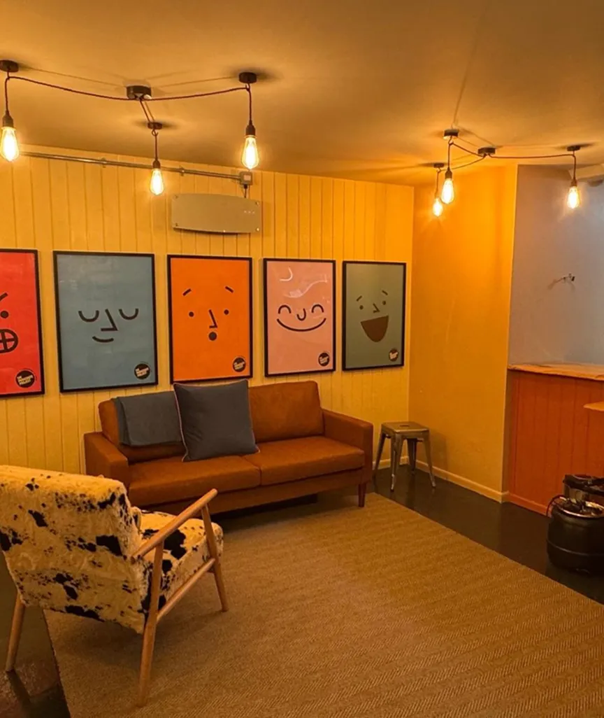 Cozy room with hanging light bulbs, a patterned chair, brown sofa, and five colorful emoticon posters.