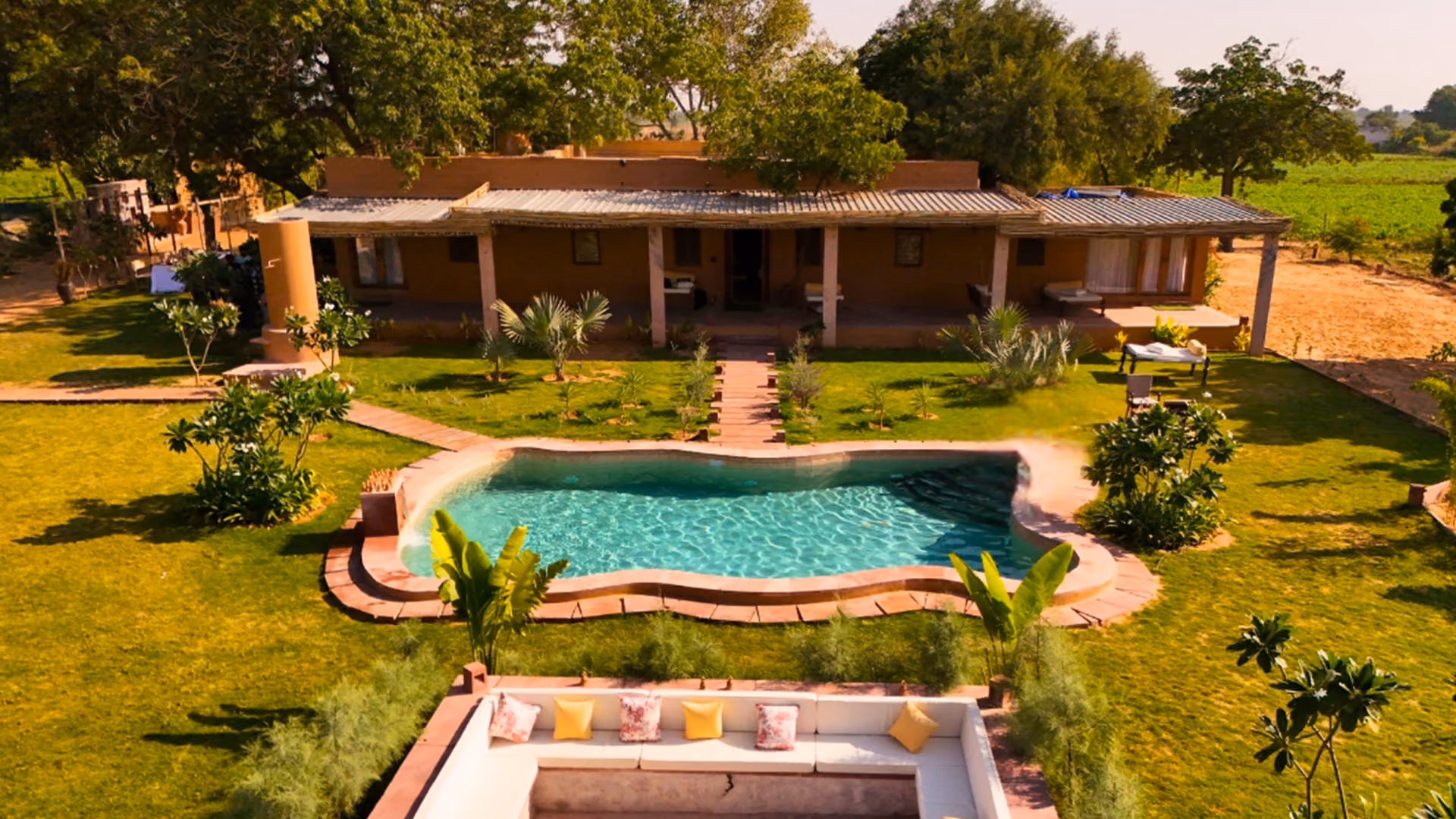 Garden villa with green lawn, a uniquely shaped swimming pool, and a cozy sunken seating area with cushions.