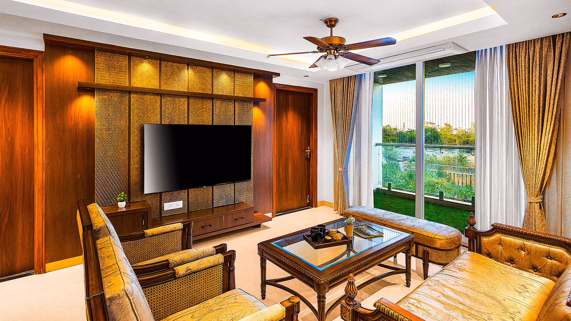 Luxurious living room with wooden furniture, glass coffee table, ceiling fan, and large window with curtains.