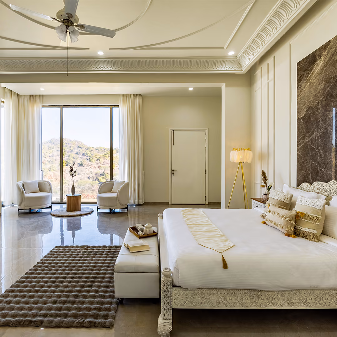 Spacious modern bedroom with white bed, decorative pillows, armchairs by large window, and floor lamp.