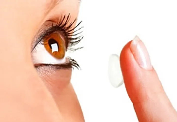 Person holding a contact lens on their fingertip close to their brown eye.