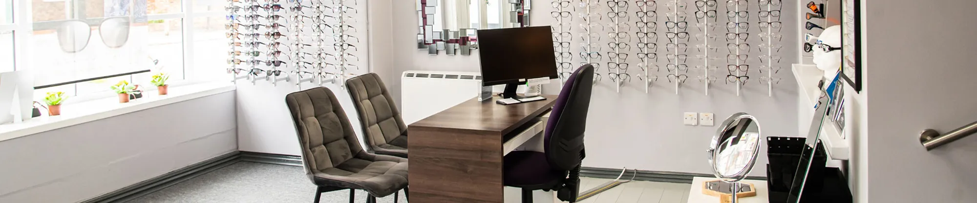Optician's dispensing area with a desk, chairs, and wall displays of eyeglasses frames