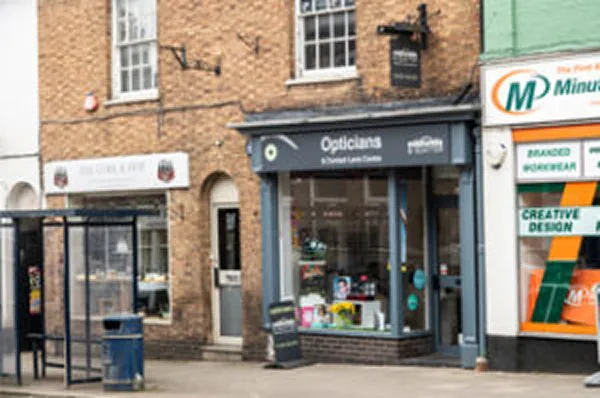 Exterior of an opticians shop on a high street next to neighbouring shops in a brick building