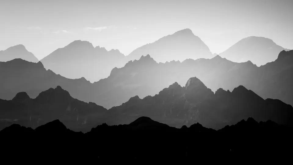 Black and white photo of layered mountain ranges fading into the distance under a clear sky.
