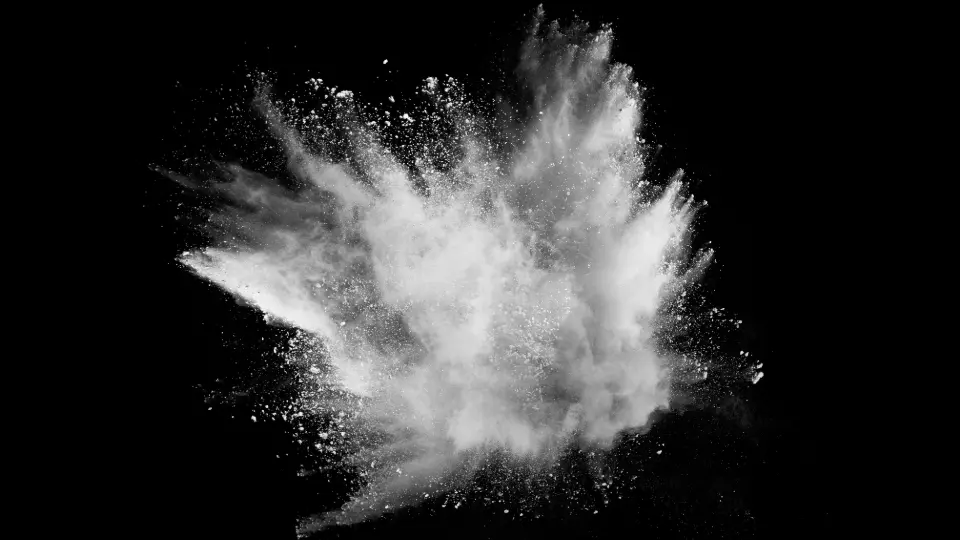 White powder explosion captured on black background, showing fine dust particles in mid-air.