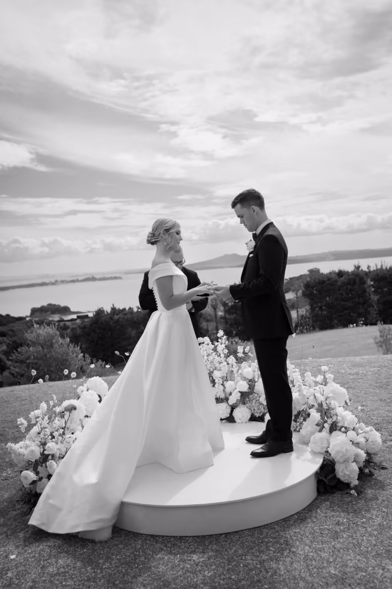 Bride and groom exchanging rings during outdoor wedding ceremony on decorated round platform.