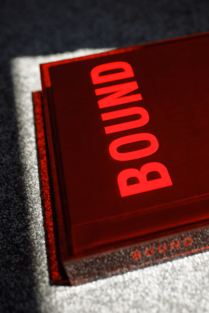 Red wedding album with the word BOUND in large capital letters on the cover, resting on a light-colored textured surface with shadows.