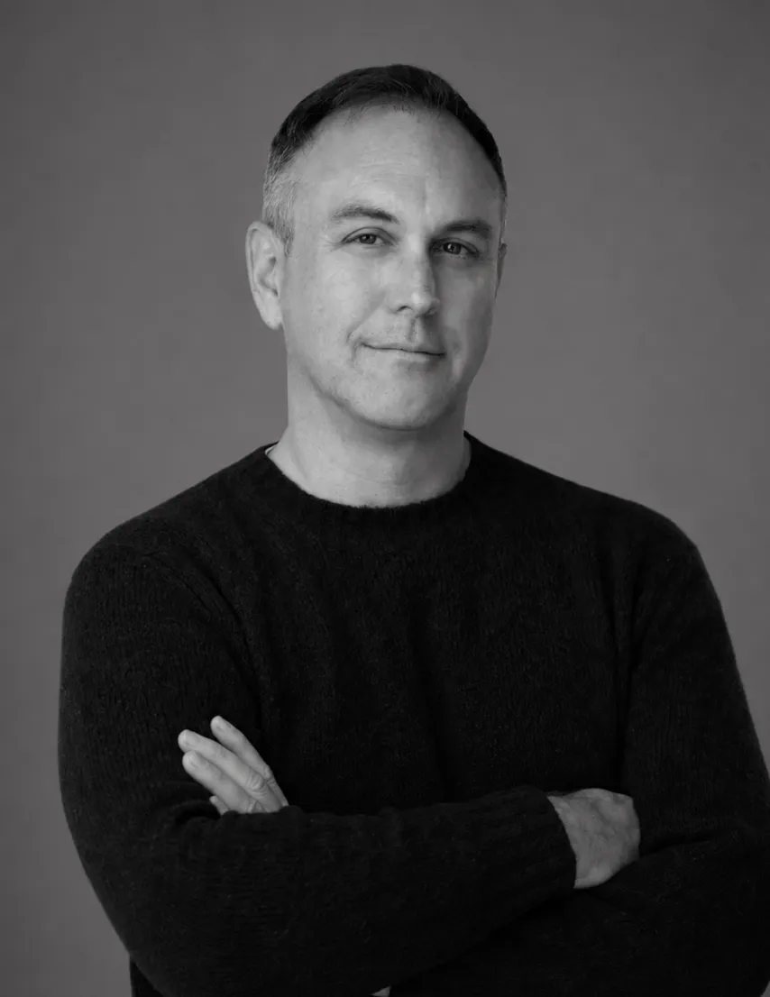 Black and white portrait of a man with short hair in a dark sweater with arms crossed.