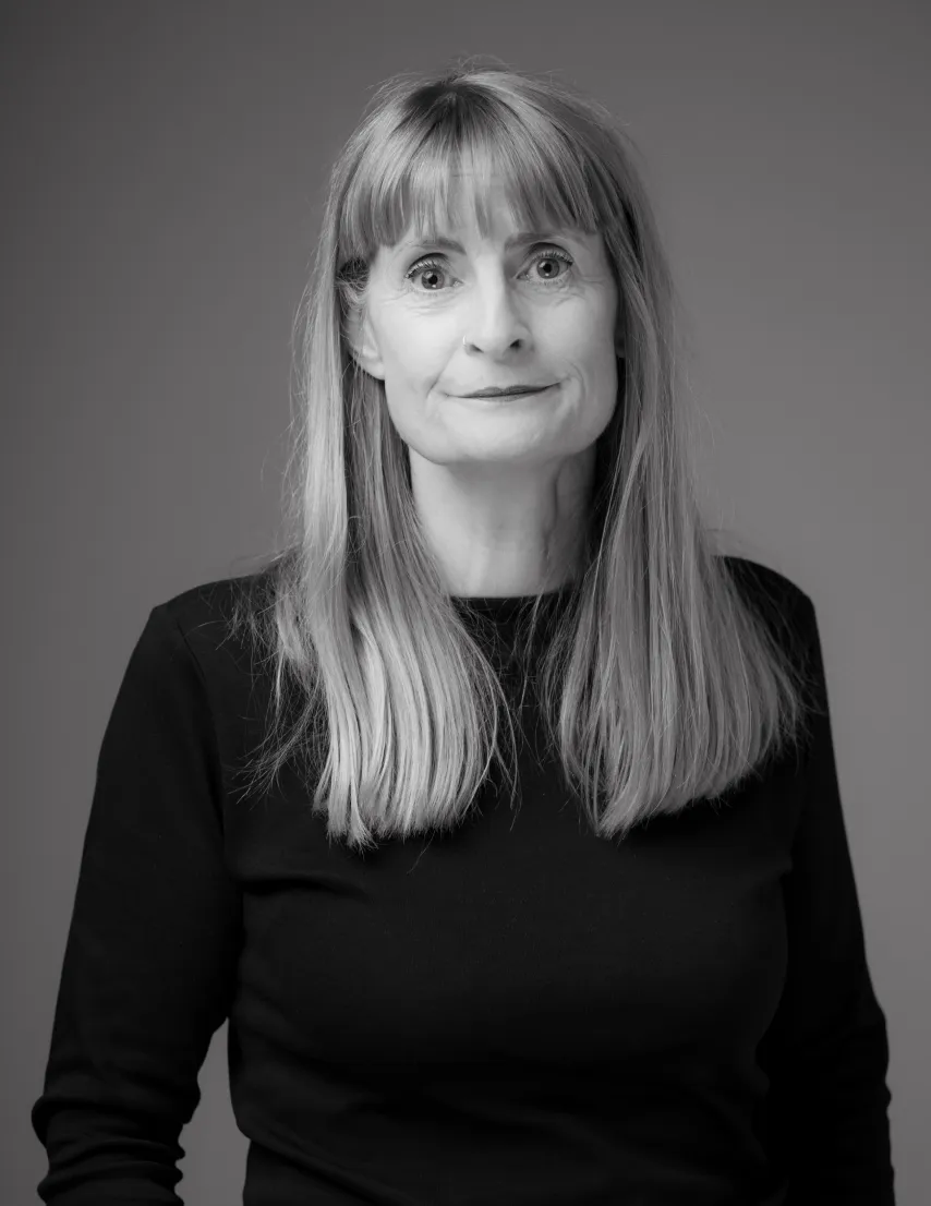 Black and white portrait of a woman with long straight hair wearing a black top, against a gray background.