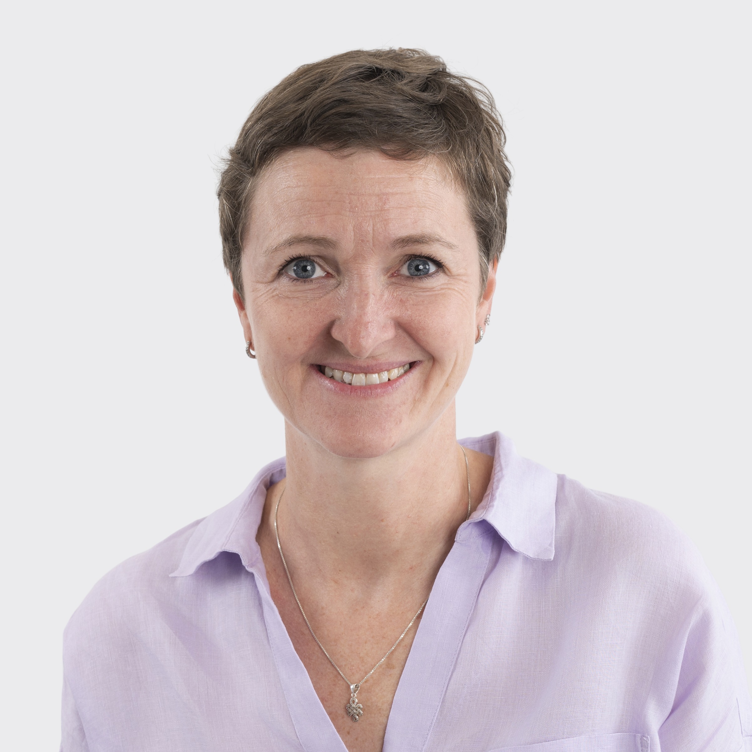 Woman with dark hair smiling, wearing a gray sweater, against a plain light background.