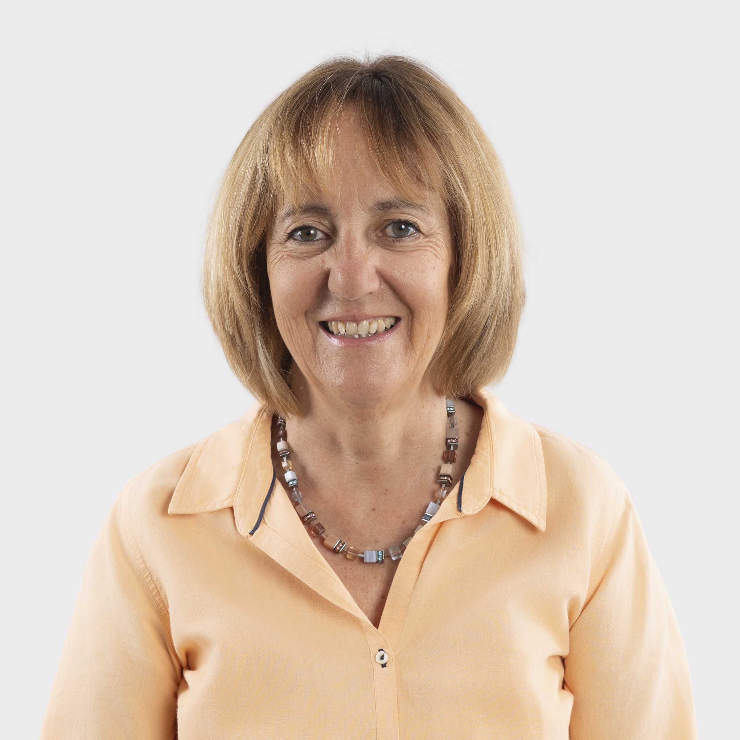 Woman with dark hair smiling, wearing a gray sweater, against a plain light background.