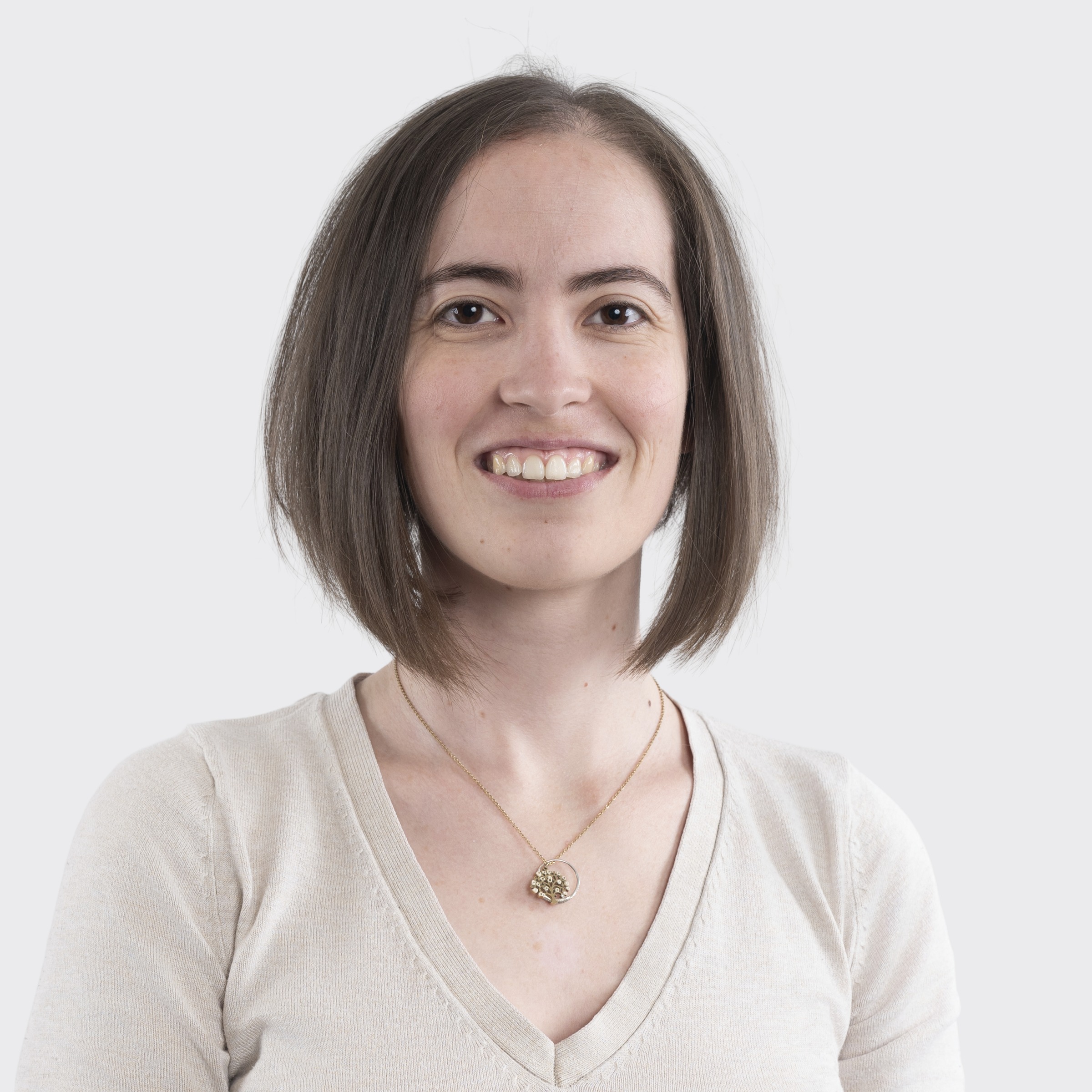 Woman with dark hair smiling, wearing a gray sweater, against a plain light background.