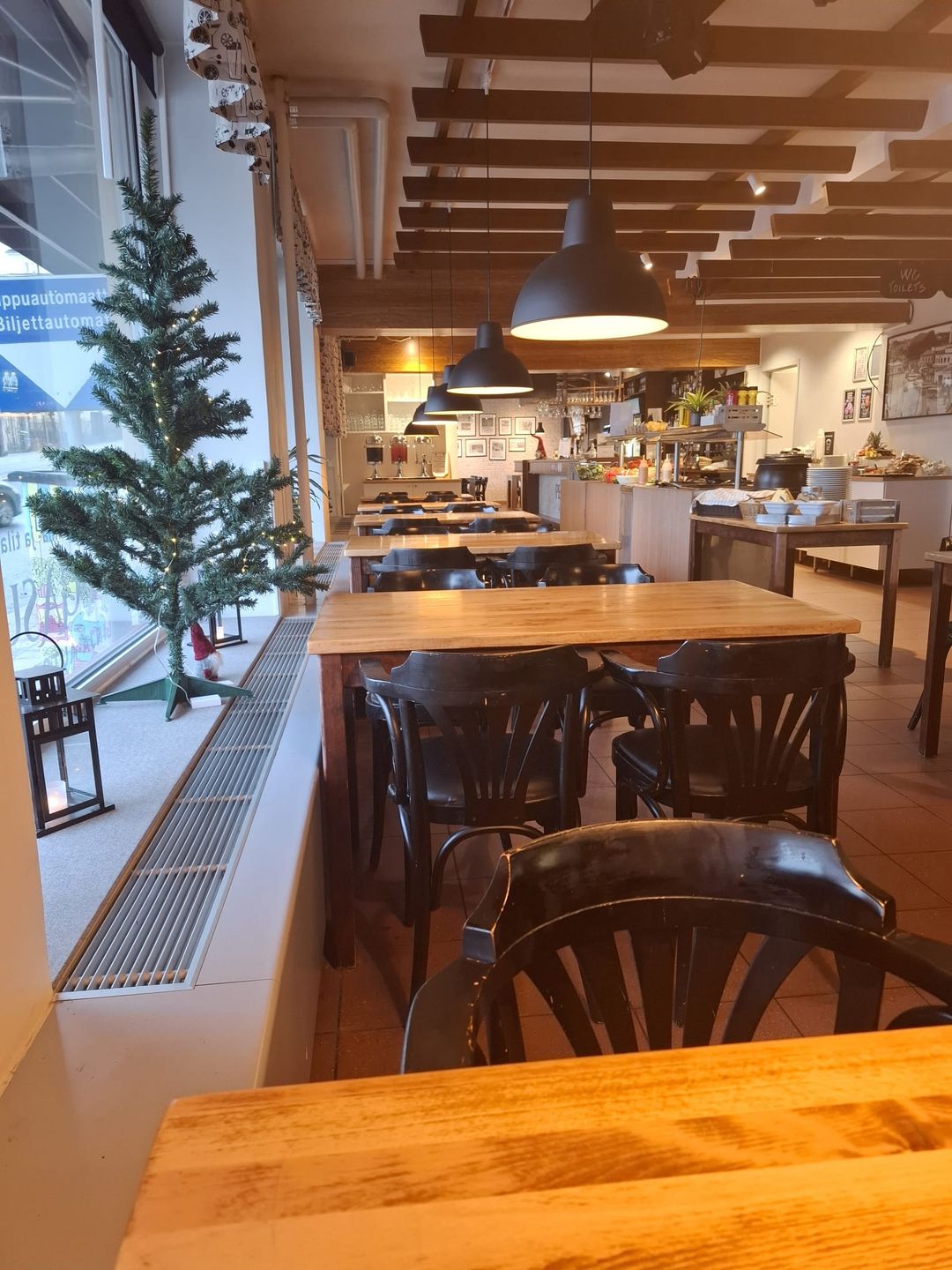 Ravintolan valoisa sali: puupöytiä, riippuvalaisimia ja buffet-tiski taustalla
