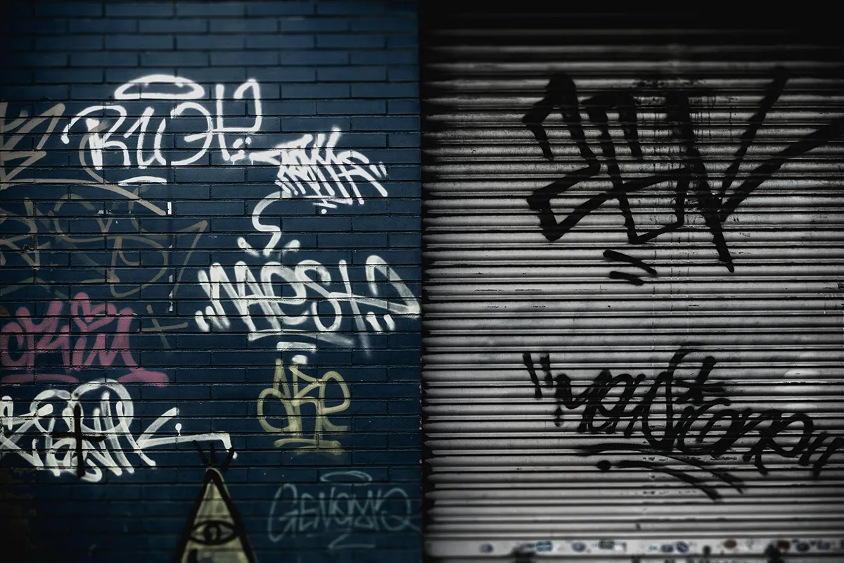 Graffitisprühereien auf einer Hauswand und einem metallenen Rolltor.