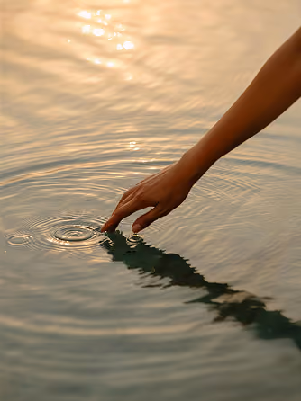 Hand touching calm water surface at sunset