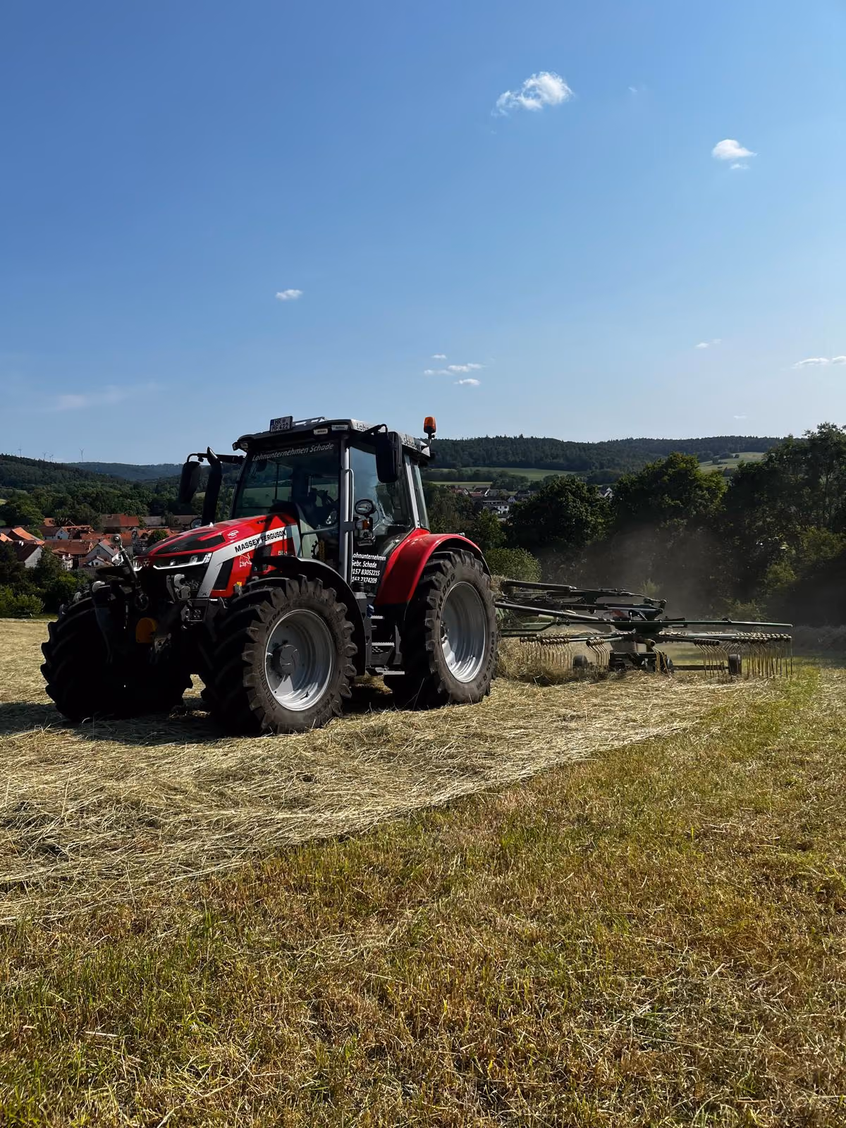 Roter Traktor fährt über ein Feld und sammelt Heu bei sonnigem Wetter mit blauem Himmel in Melsungen. Schwaden oder Mulchen für Ernte & Pflege.