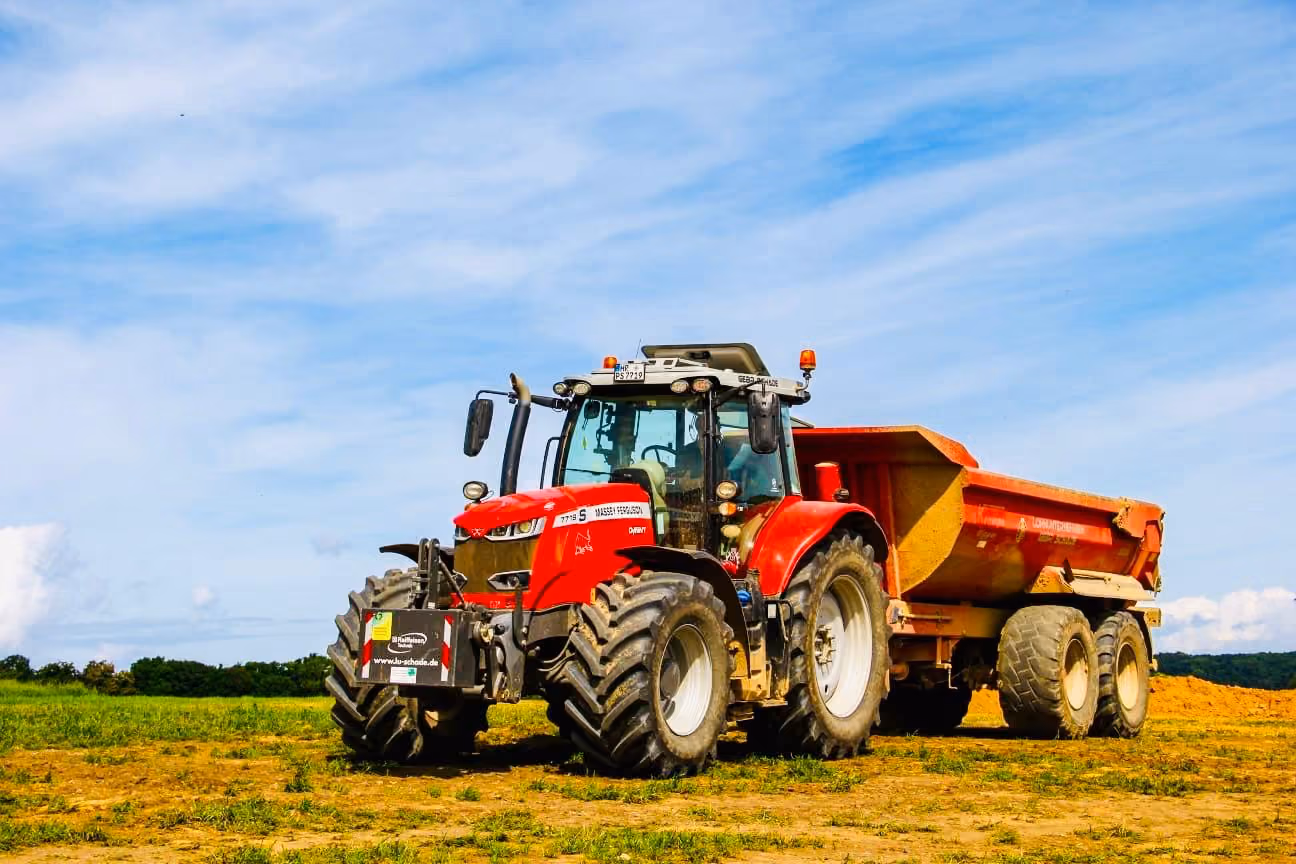 Roter Traktor vom Lohnunternehen Gebr. Schade mit Erdmulde anhänger auf Feld unter blauem Himmel an einem sonnigen Tag in Bad Hersfeld (Hessen)