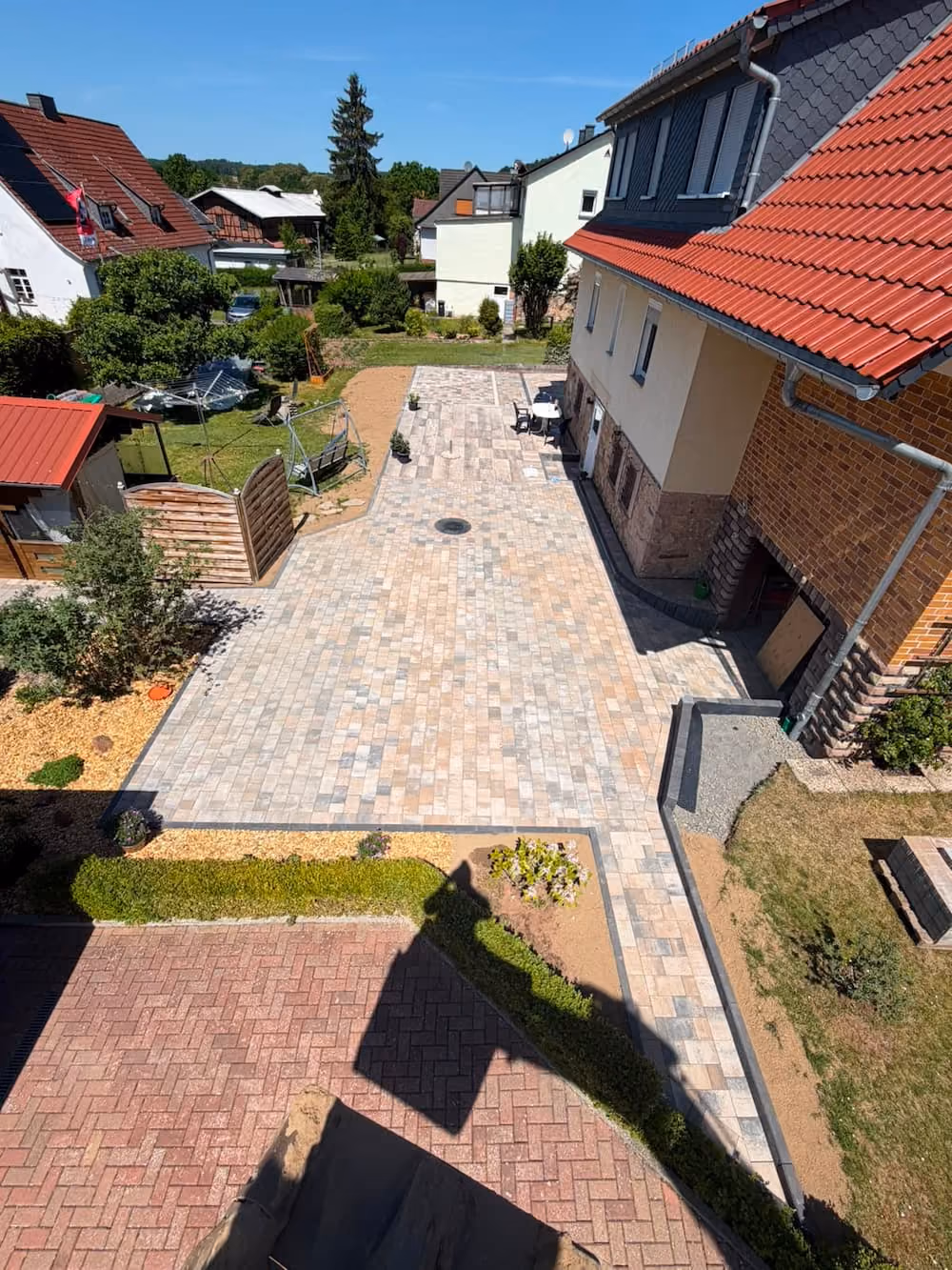 Hof in Rotenburg an der Fulda mit Neu gepflasterter Einfahrt und Bereich neben Haus mit roten Dächern und Garten mit Büschen. Garten- Landschaftsbau Referenz Gebr. Schade
