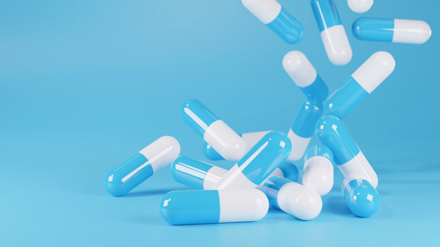 Capsules bleues et blanches tombant sur une surface bleue unie.